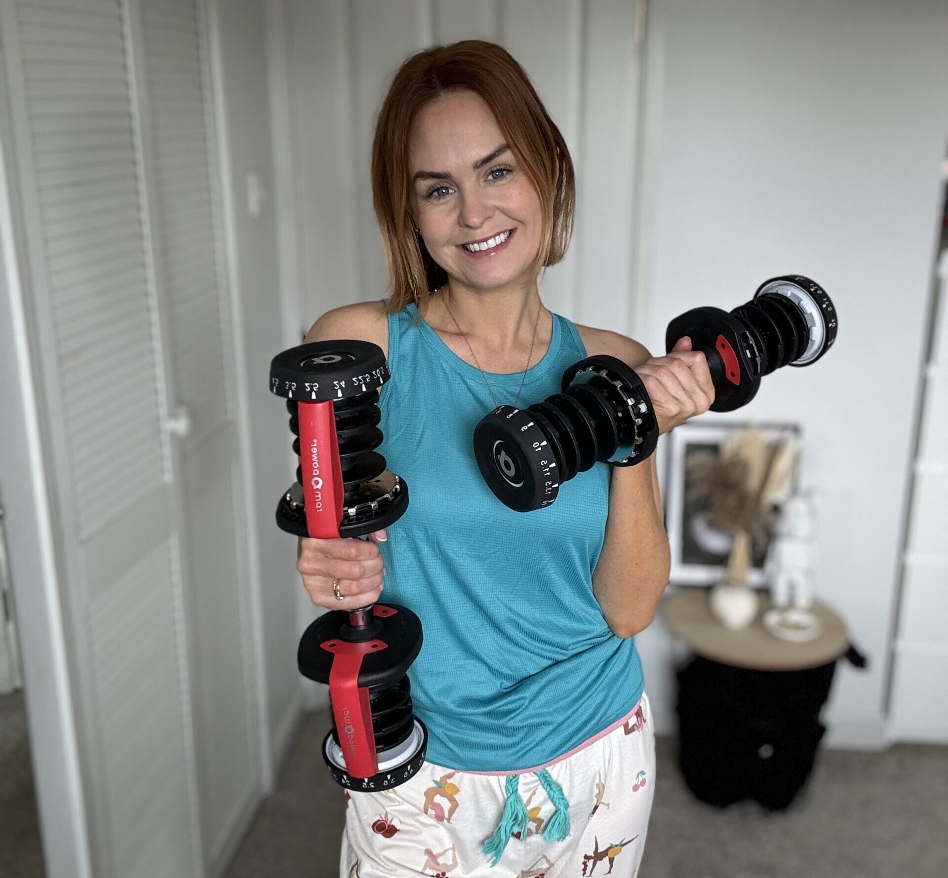 Maryrose, dressed in comfy pajamas, lifts two dumbbells, embodying a fun mix of home comfort and fitness enthusiasm all with a stoma bag!