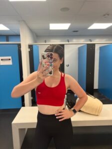 Amy captures a selfie in the gym, wearing a red sports bra, embodying strength and motivation for those with a stoma!