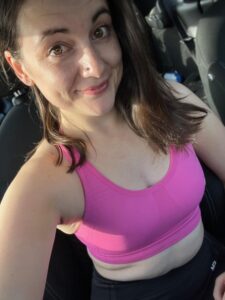 Amy takes a selfie in a pink sports bra in her car, radiating a blend of comfort and athleticism.