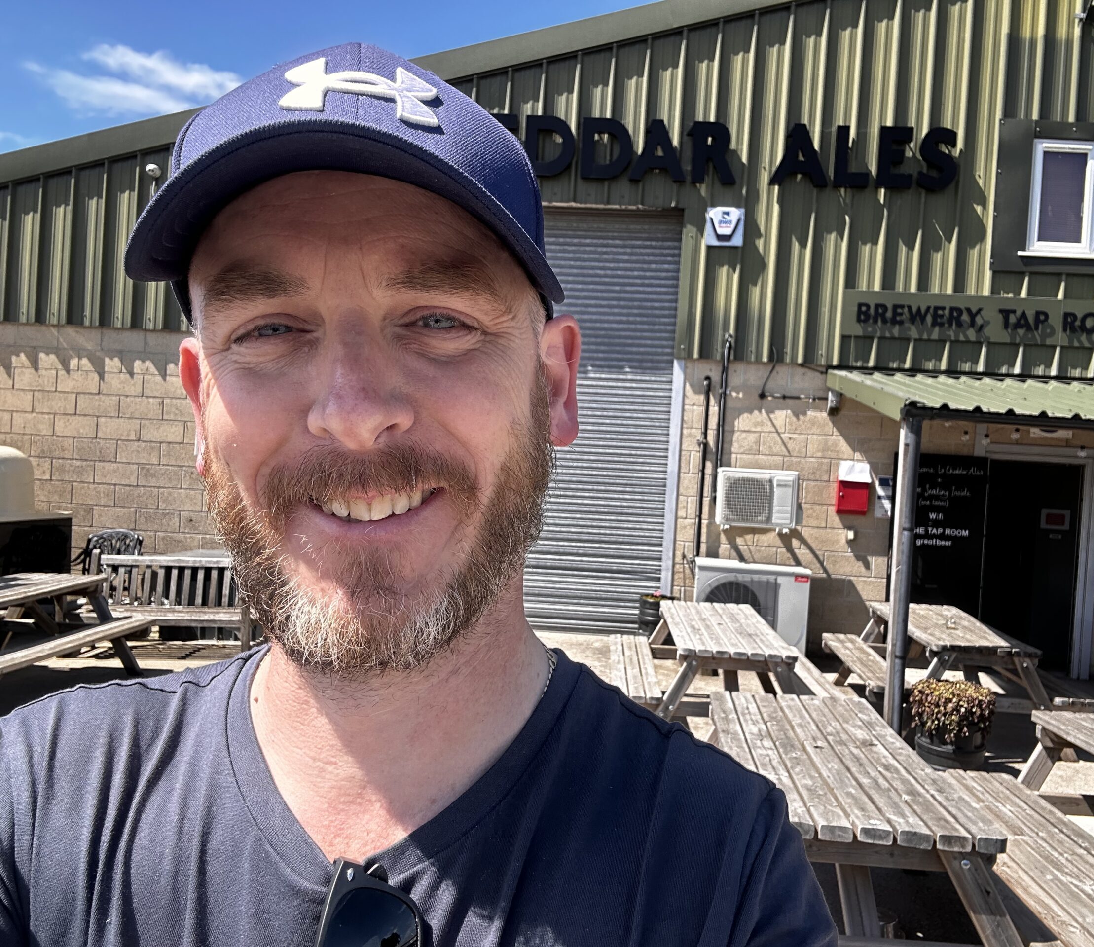 Chris, wearing a hat and a blue shirt, smiling and enjoying a sunny day outdoors.